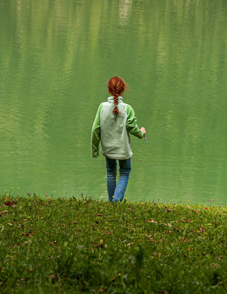Mädchen mit rotem Zopf an einem See mit grünem Wasser / © Foto: Georg Berg