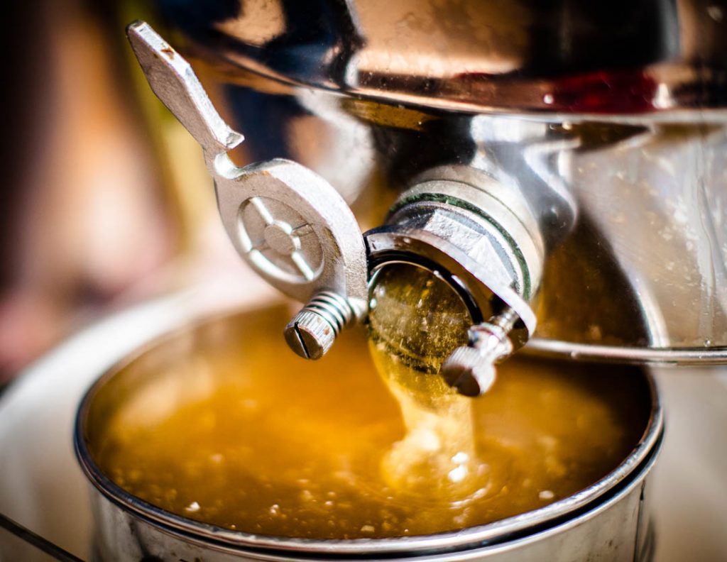 Honey is flowing from the honey extractor outlet through a strainer / © Foto: Georg Berg