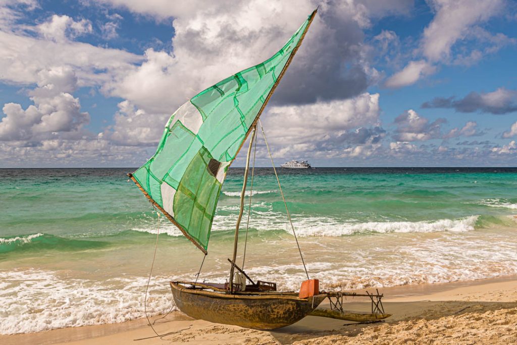 Polynesisches Segelboot (Prau) am Strand der Insel Yanaba aus Papua Neuguinea. Im Hintergrund ist das Expeditionsschiff True North zu sehen