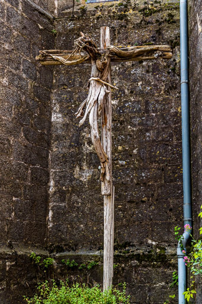 Vor der Kirche Sainte Marie de Mourèze steht ein Kreuz, das der Künstler Emmanuel Cometto aus unbearbeitetem Holz geschaffen hat / © Foto: Georg Berg
